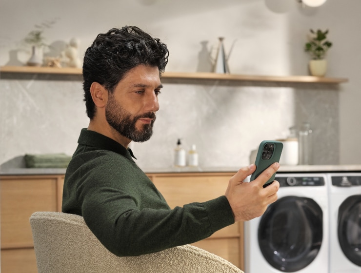 A man sitting on chair with phone in hand and washing machine in background
